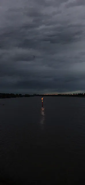 Eine Leuchtboje im Wasser, darüber dunkle Wolken